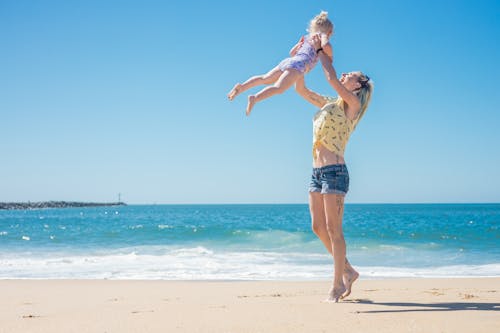 ビーチの砂の上に立っている間、空中に娘を投げる女性