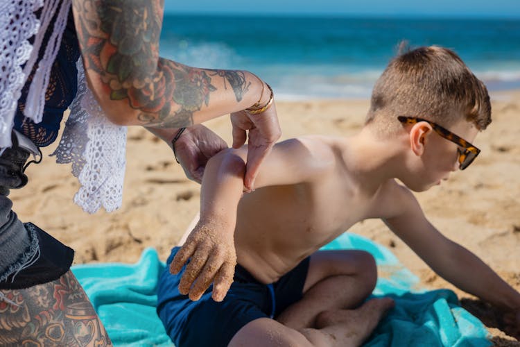 A Person's Hands Putting Sunscreen On A Boy's Skin