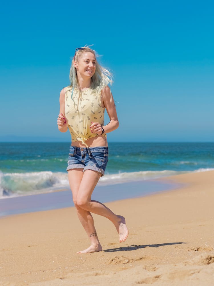 A Woman In Denim Shorts Running On The Beach Sand