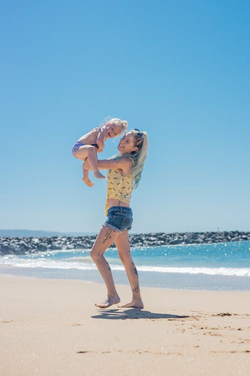 A Woman Standing on the Beach while Carrying Her Daughter