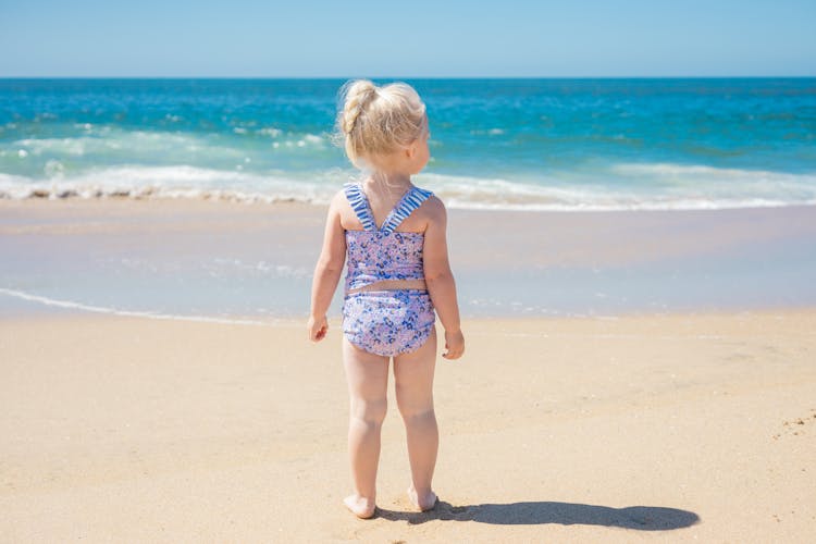 Blonde Girl In Floral Swimwear Standing On Beach Sand