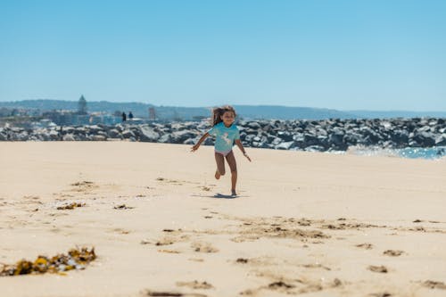 Photograph of a Kid in a Blue Shirt Running on the Sand