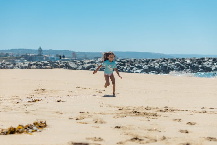 Photograph Of A Kid In A Blue Shirt Running On The Sand