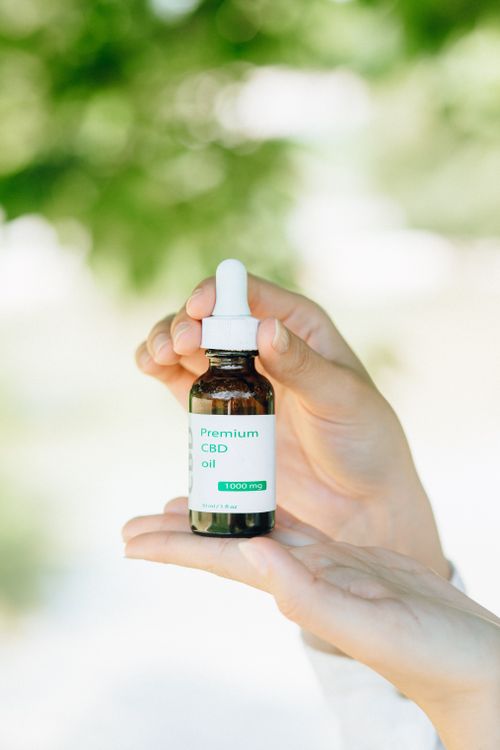 Free A close-up of a CBD oil bottle held by hands, set against a natural outdoors background. Stock Photo