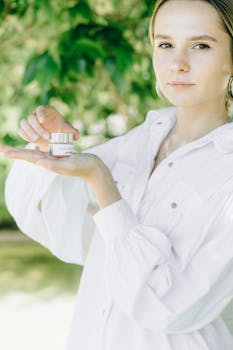 A young woman holds a skin cream container in a serene outdoor setting, showcasing beauty and skincare.