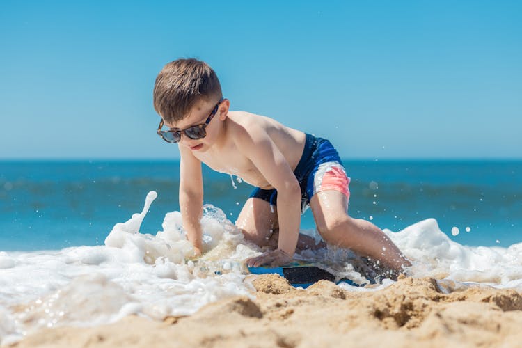A Boy In Blue Shorts Sitting On Beach Shore