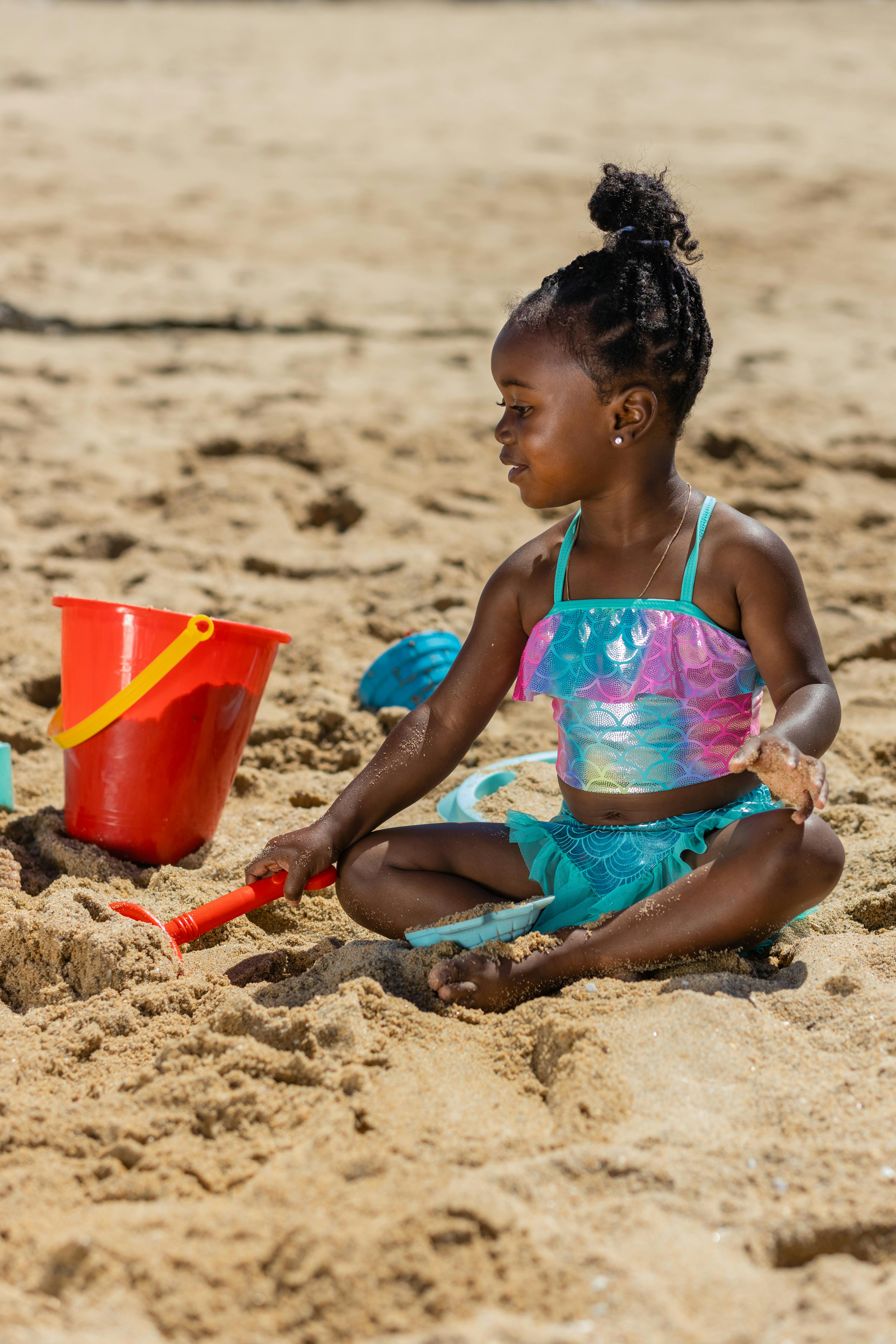 a cute girl in blue swimsuit sitting on the beach sand