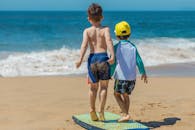 两个孩子在沙滩上玩冲浪板，在海边享受阳光明媚的一天