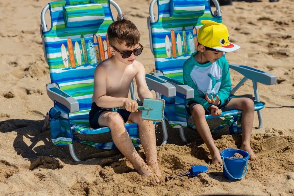 Two boys enjoying a sunny day at the beach with chairs and sand toys.