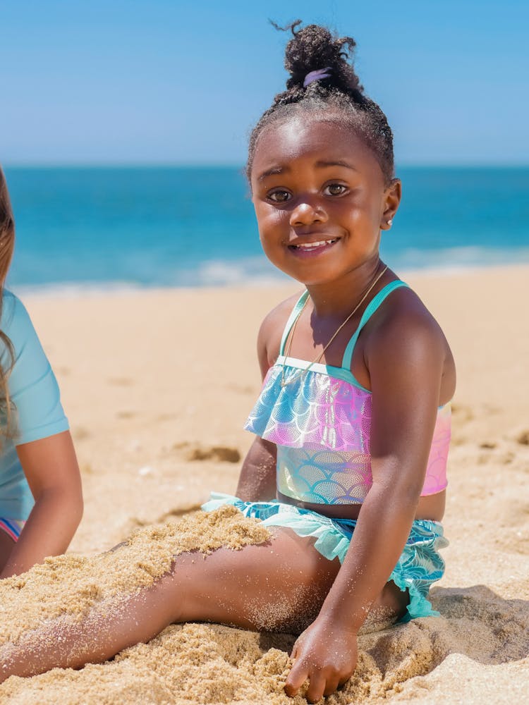 A Young Girl In Mermaid Style Swimsuit Sitting On The Sand