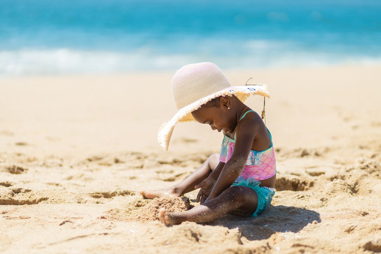 Toddler in a sun hat playing in the sand at the beach