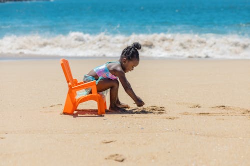 Little Girl Sitting on Orange Plastic Chair on Beach