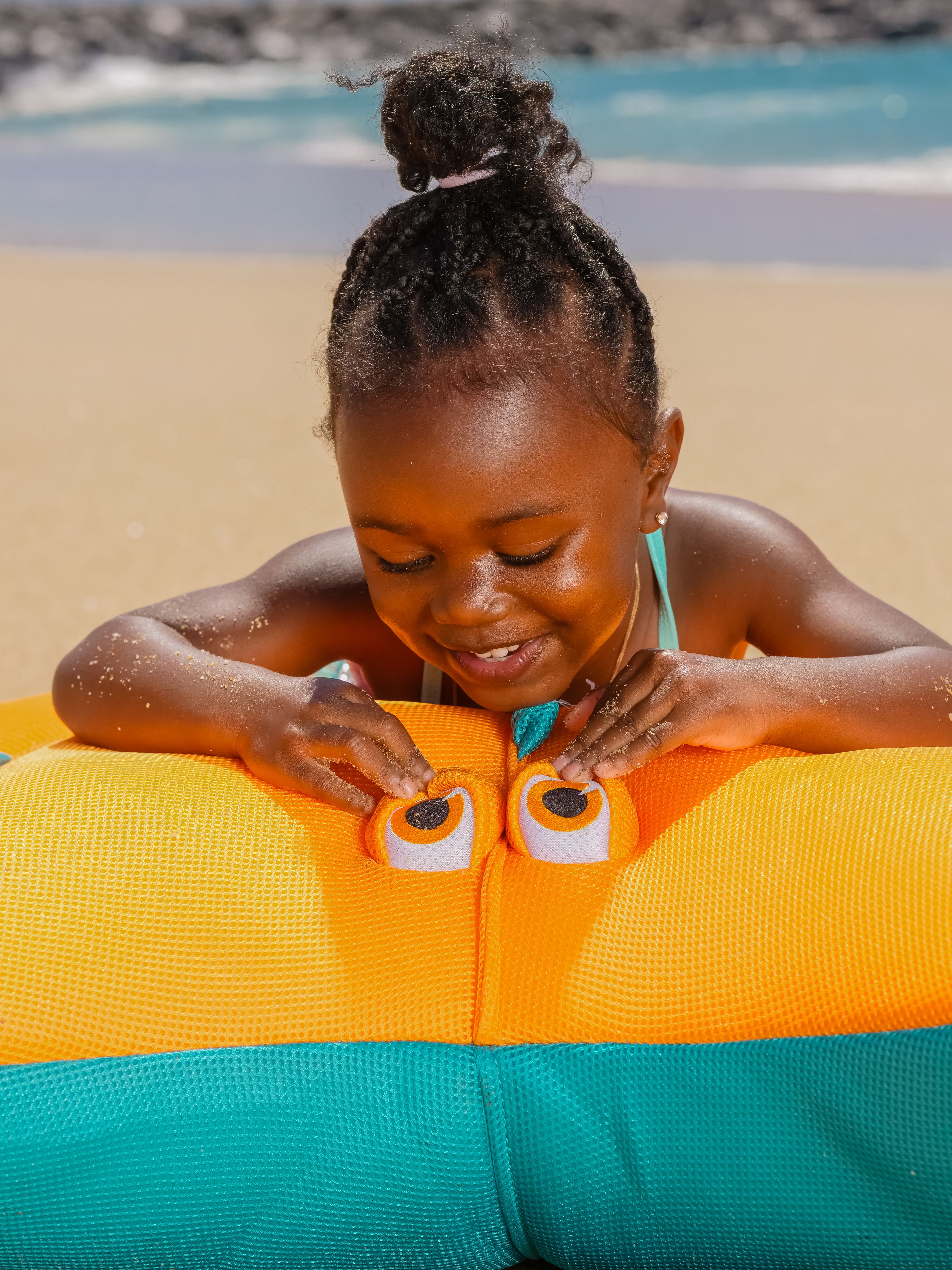 Smiling child enjoys a colorful inflatable toy on a sunny beach day.