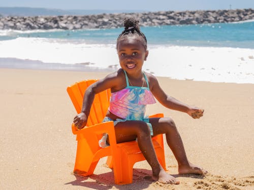 Cute Little Girl Sitting on Orange Plastic Chair on Beach