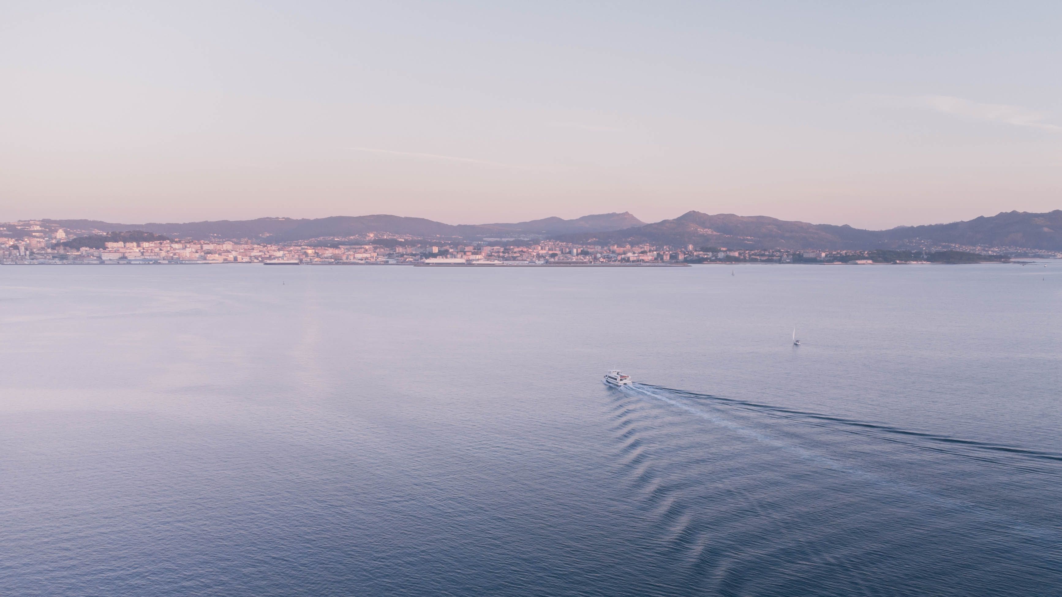 Stunning aerial view of a coastal city with boats sailing at sunset, showcasing tranquil ocean waves.