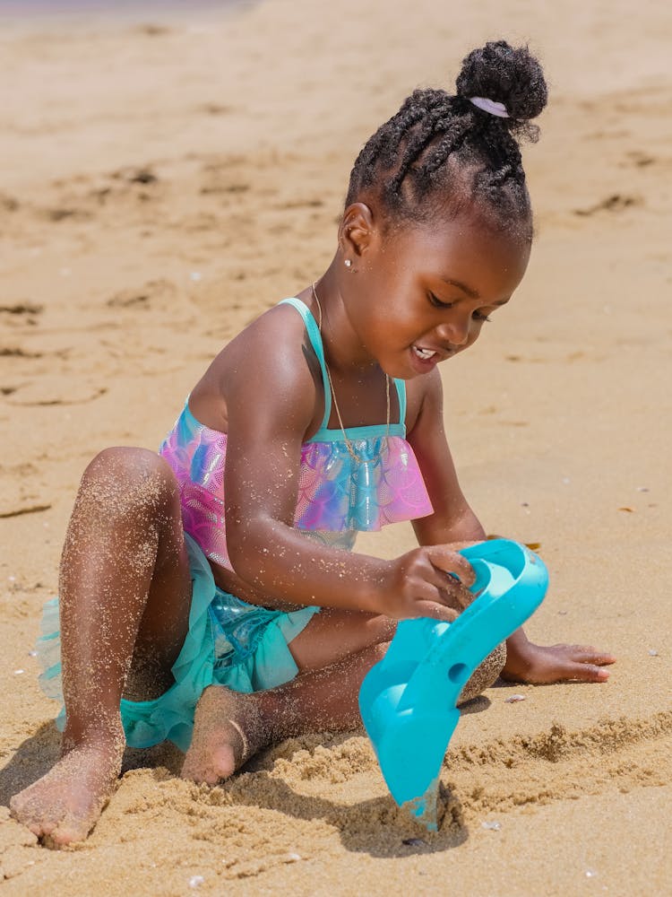 A Young Girl Sitting On The Beach Sand While Holding Her Toy