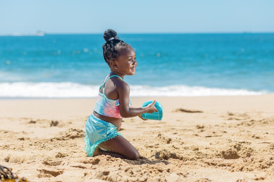 Adorable child enjoys a sunny day at the beach playing in the sand with toys.