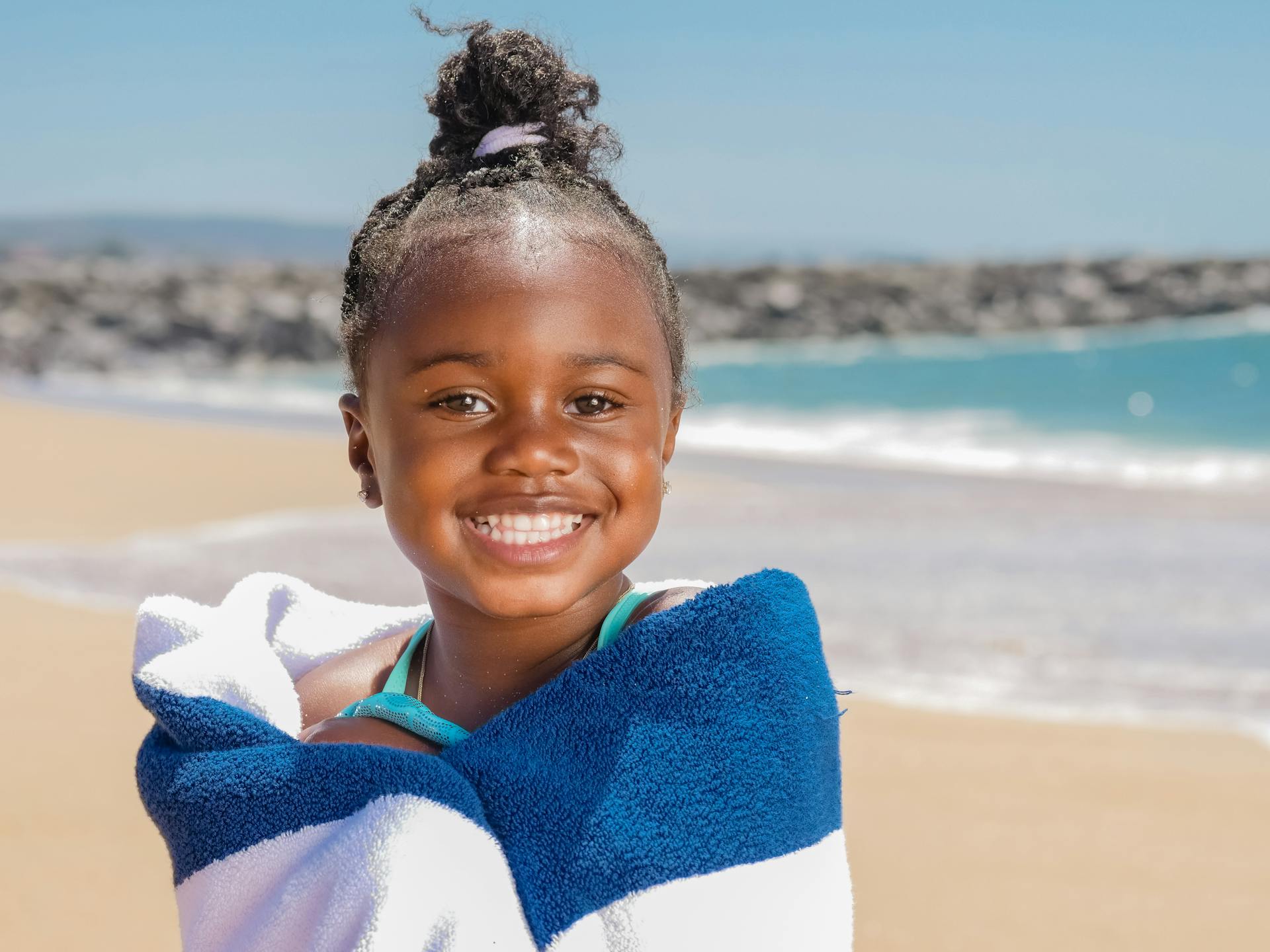 Joyful child wrapped in a towel enjoying a sunny day at the beach with a bright smile.