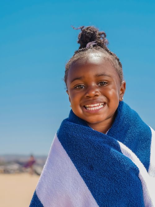 Free A joyful child wrapped in a blue and white towel enjoying a sunny day at the beach. Stock Photo