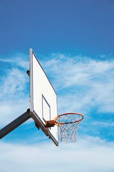 Low-angle shot of a basketball hoop outdoors against a bright blue sky.