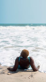 A person enjoying a serene moment lying on a sandy beach with gentle ocean waves in Lagos, Nigeria.