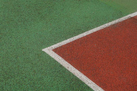 Close-up view of a textured sports court with green and red sections separated by a white line.