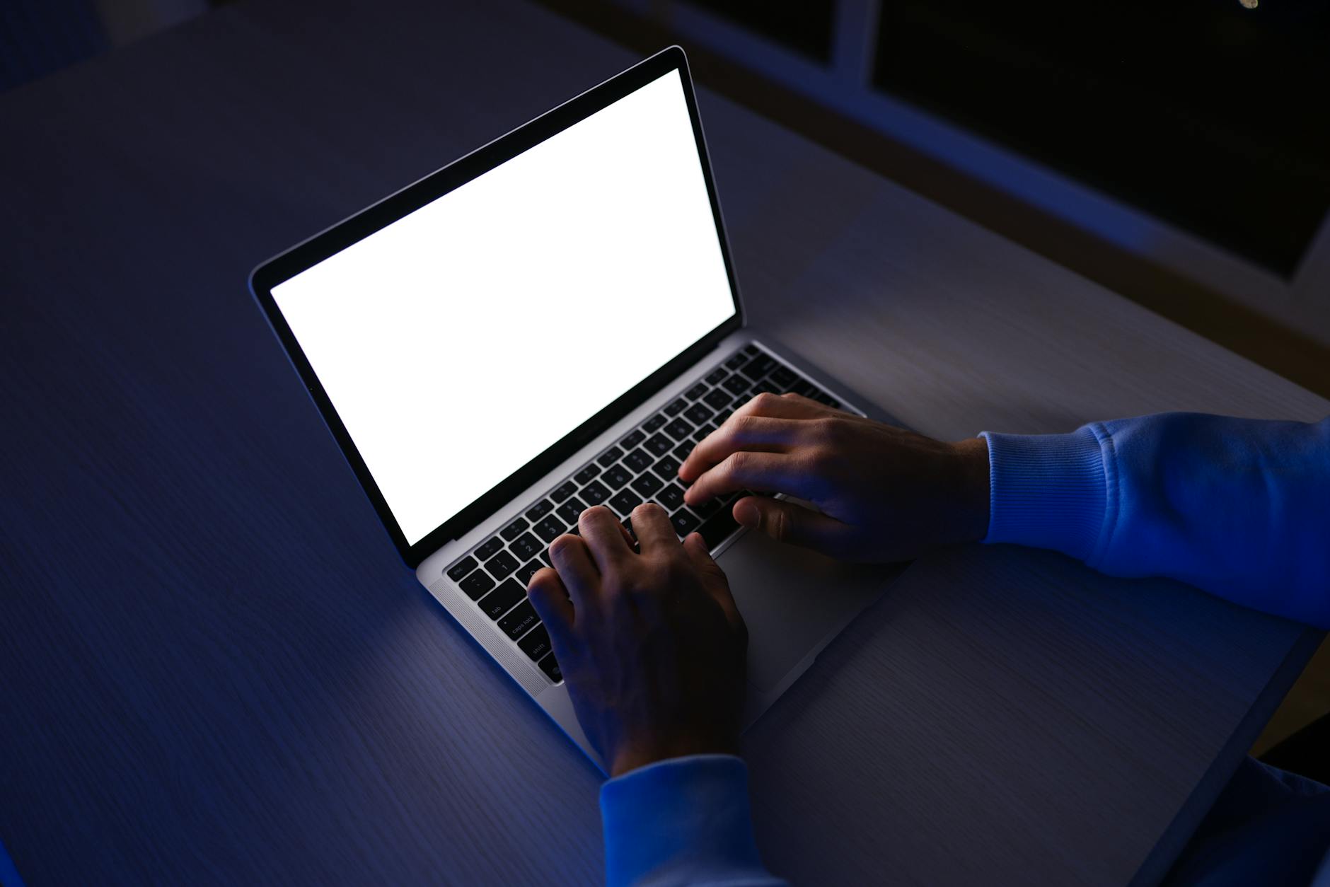 Person working late on a laptop with a blank screen, illuminated by screen light.