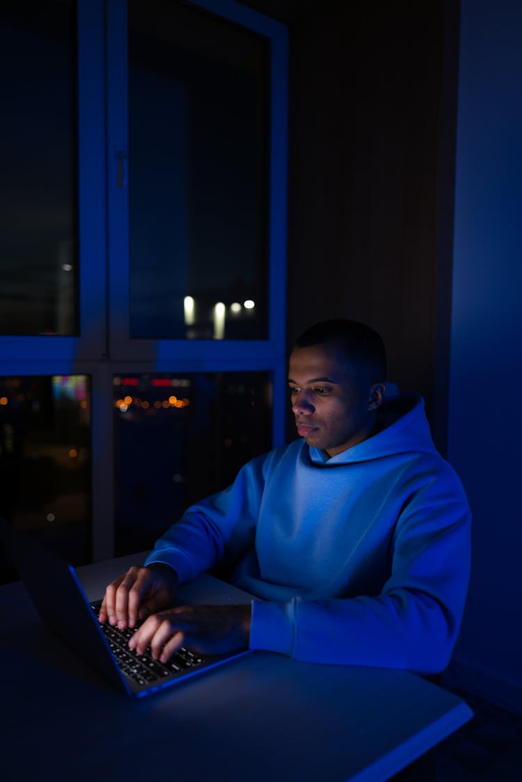 A Man Typing On A Laptop In The Dark 