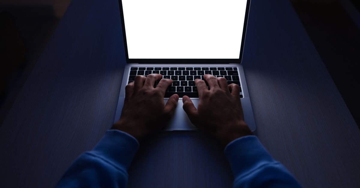 Hands typing on a laptop with a blank white screen in a dimly lit room.