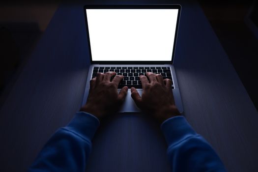 Hands typing on a laptop with a blank white screen in a dimly lit room.
