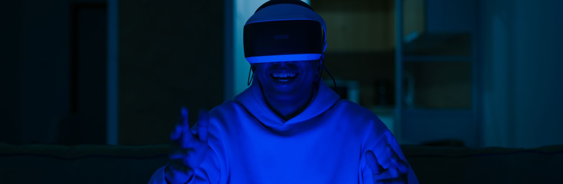 Man enjoying virtual reality gaming indoors with blue light ambiance.