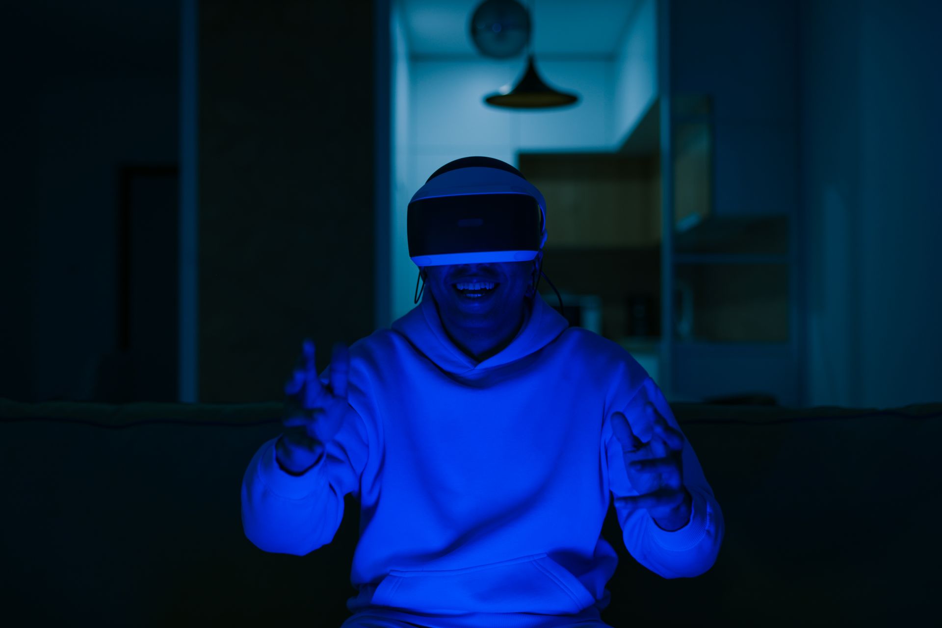 Man enjoying virtual reality gaming indoors with blue light ambiance.