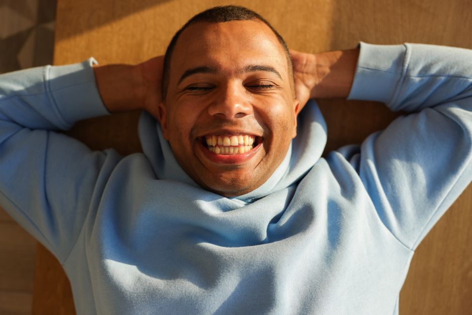 Fotomural Primer plano de un hombre alegre en un hoodie azul acostado, sonriendo con los ojos cerrados.