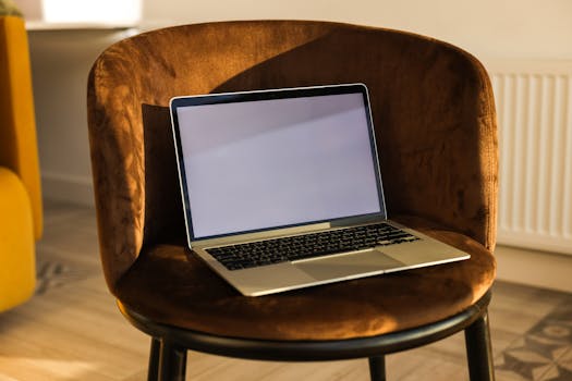 Laptop with a blank screen placed on a brown velvet chair in a bright room.