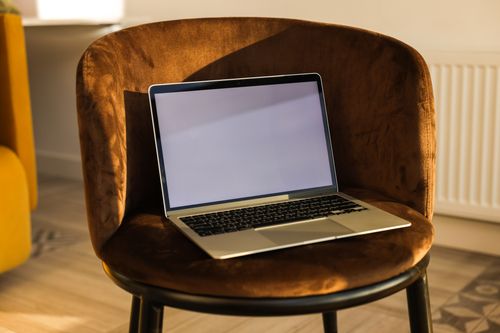 Free Laptop with a blank screen placed on a brown velvet chair in a bright room. Stock Photo