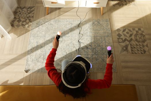 Top view of a woman using VR headset and controllers indoors under sunlight.