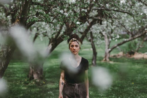Free Woman in Black Shirt with Curly Hair Standing on Grass Near Trees Stock Photo