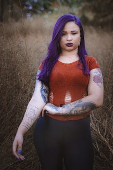 Portrait of a woman with purple hair and tattoos in a natural outdoor setting.