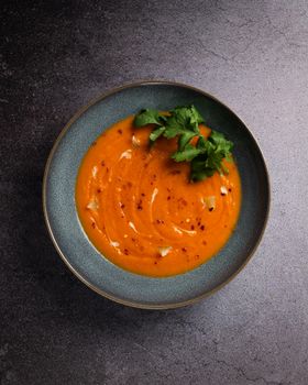 Top view of a delicious creamy carrot soup garnished with fresh cilantro leaves.