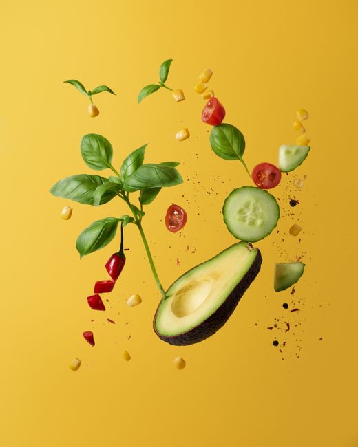 Vibrant composition of floating avocado, vegetables, and herbs on a yellow background, perfect for creative food concepts.