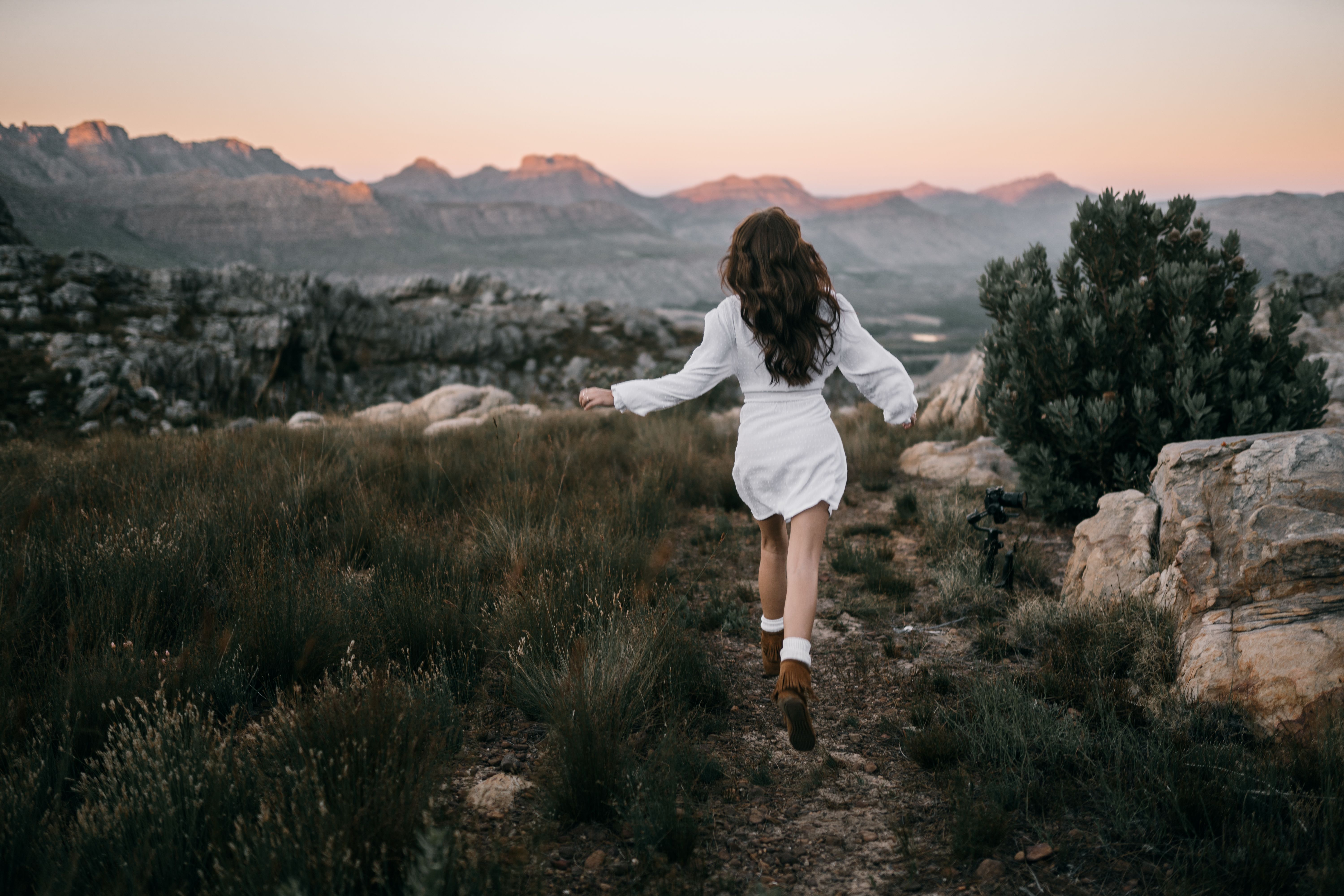 A woman in white runs through a scenic mountain path at dusk, evoking wanderlust.