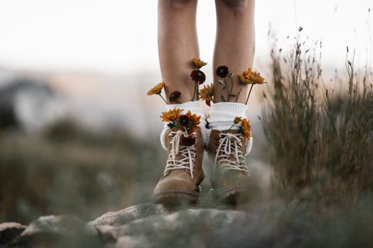 Brown boots adorned with colorful flowers, set against an outdoor natural backdrop.
