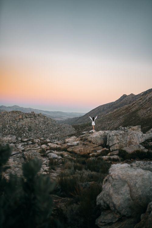 Free A lone adventurer stands atop rocky terrain under a pastel sky, embracing twilight serenity. Stock Photo