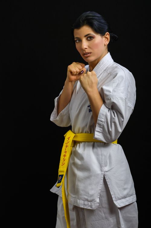 Free Confident woman in karate attire with yellow belt posing on a black background. Stock Photo