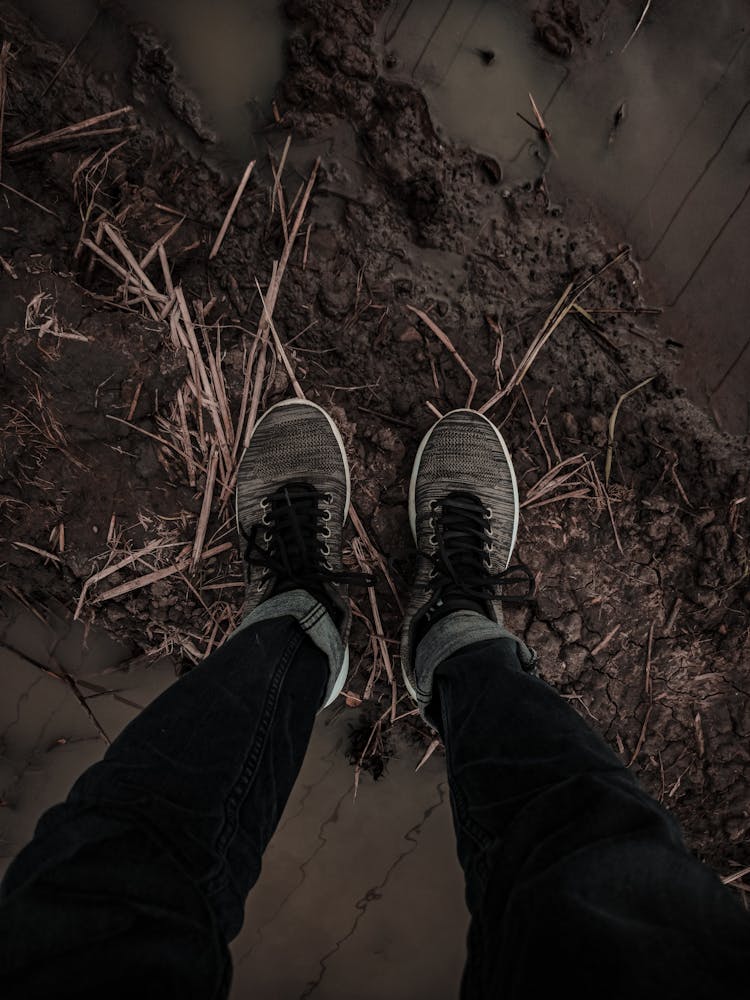 High-Angle Shot Of A Person Wearing Sneakers Standing By A Muddy Puddle