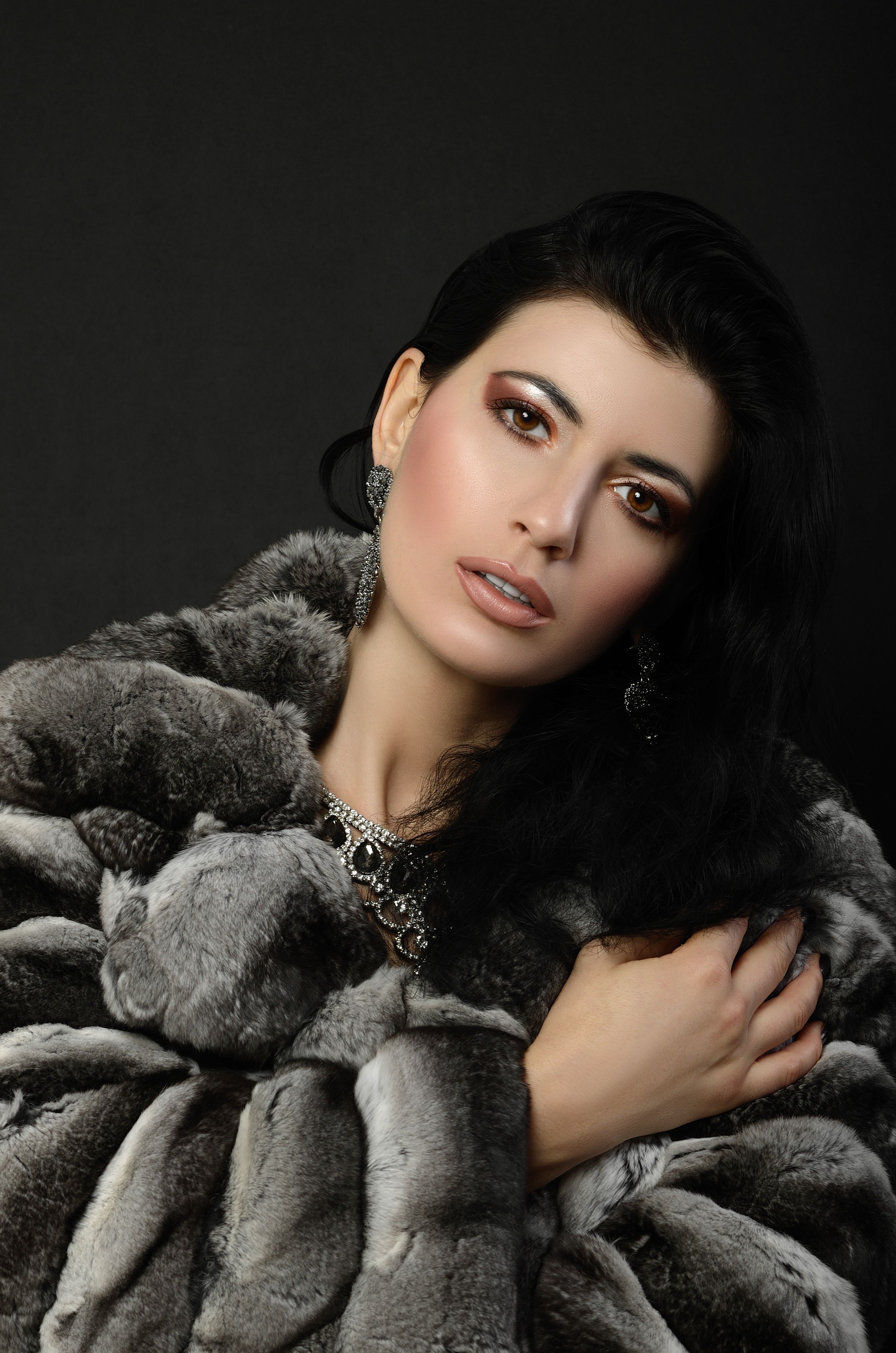 Sophisticated woman in faux fur coat with elegant jewelry in a studio setting.