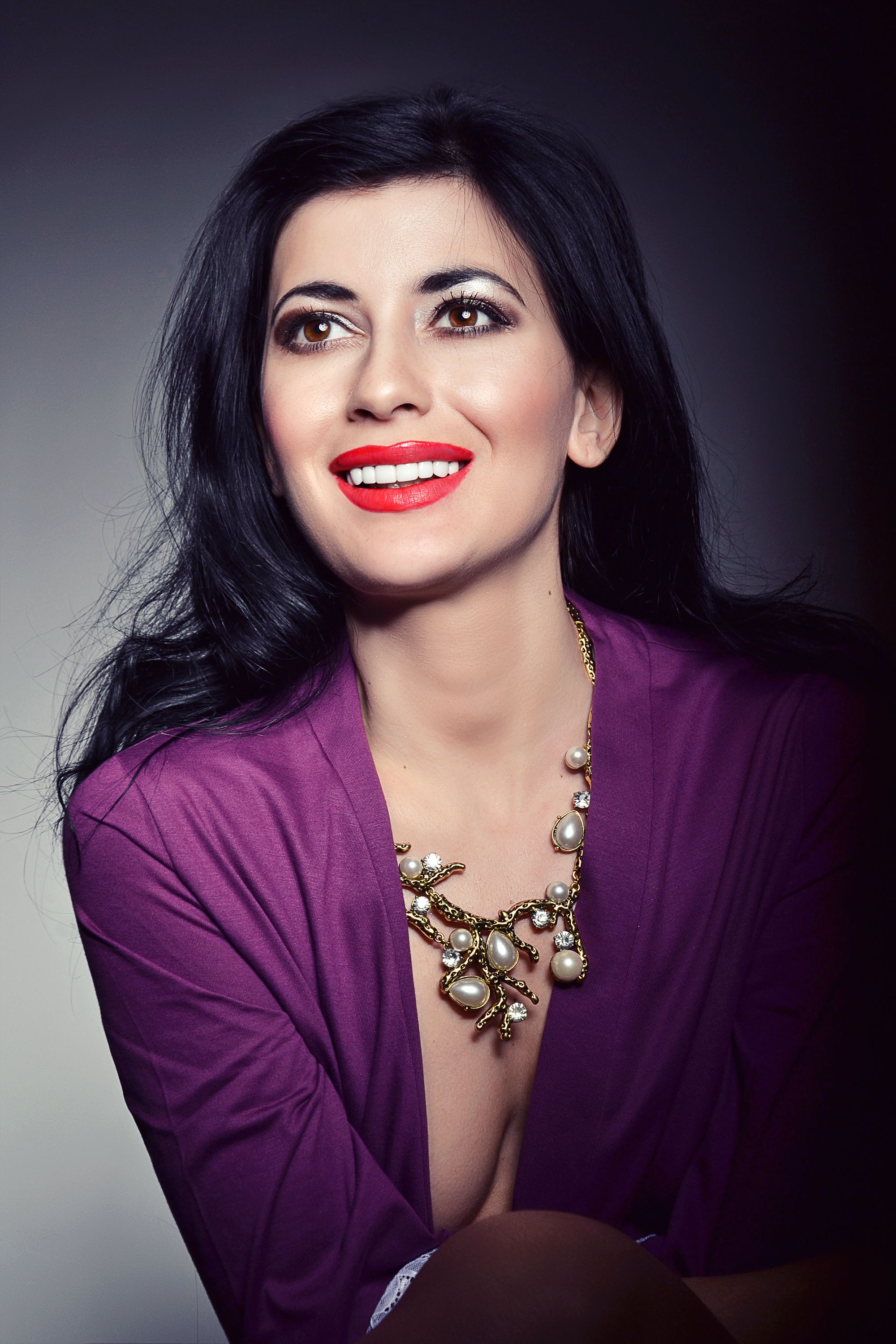Portrait of a smiling woman in purple attire and jewelry, exuding elegance.