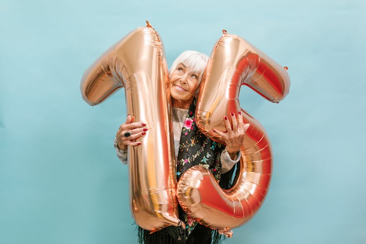A Happy Elderly Woman Celebrating Her Birthday While Holding A Huge Balloon Numbers