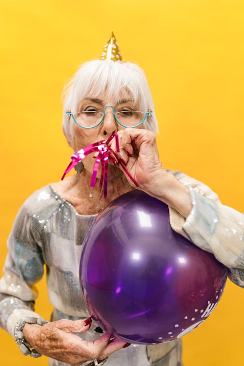 Elderly Woman with a Blower and a Birthday Balloon