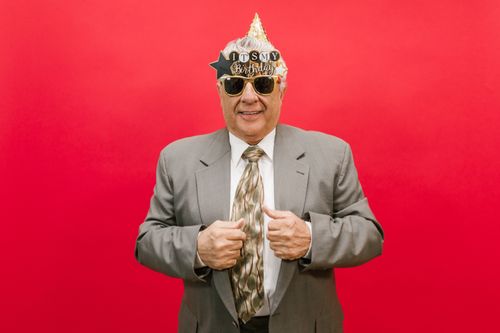 Free Cheerful elderly man in a gray suit celebrating birthday in studio with festive accessories. Stock Photo